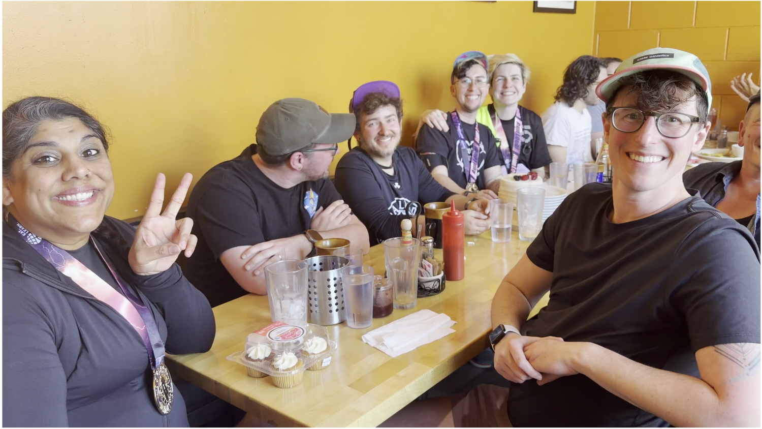 Group of people sitting around a table with drinks and snacks, smiling at the camera.